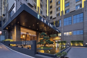 Una entrada de hotel moderna con un paseo techado, un elemento acuático y un cartel con el nombre del hotel.