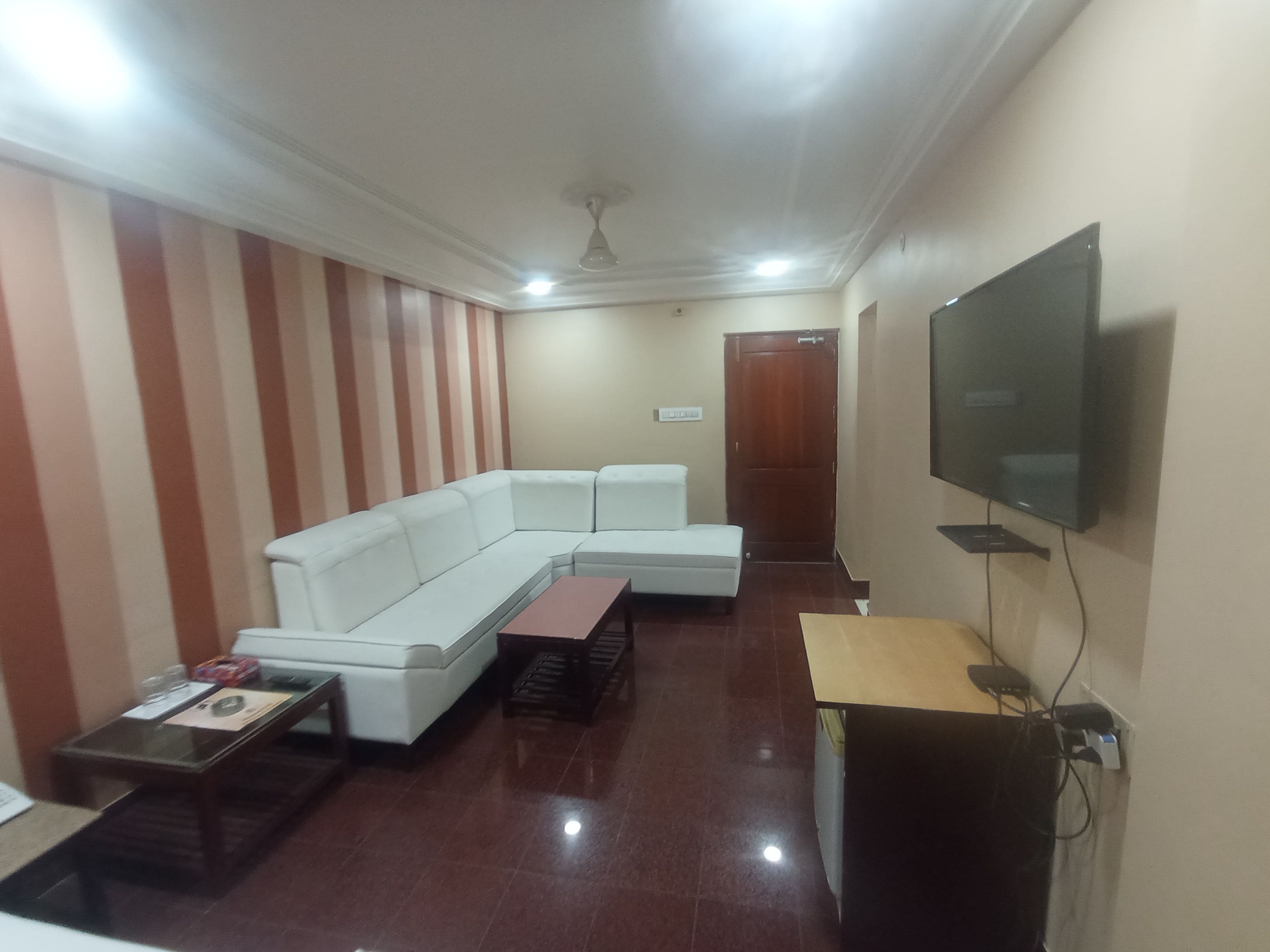 Una sala de estar con un sofá modular, un televisor de pantalla plana montado en la pared y una mesa de centro de madera.