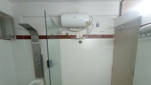 Um chuveiro pequeno e fechado, com porta de vidro, parede revestida de azulejos brancos e aquecedor de água instalado no teto branco.