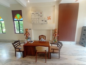 A conference room with a wooden table, four chairs, a wall-mounted electrical panel, and a large window with a view.
