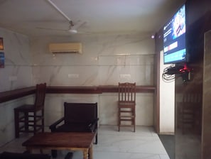 A room with a television mounted on the wall, a ceiling fan, and a wooden table.