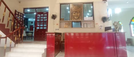Un hall d’hôtel avec un escalier, un comptoir d’accueil et une statue de Bouddha.