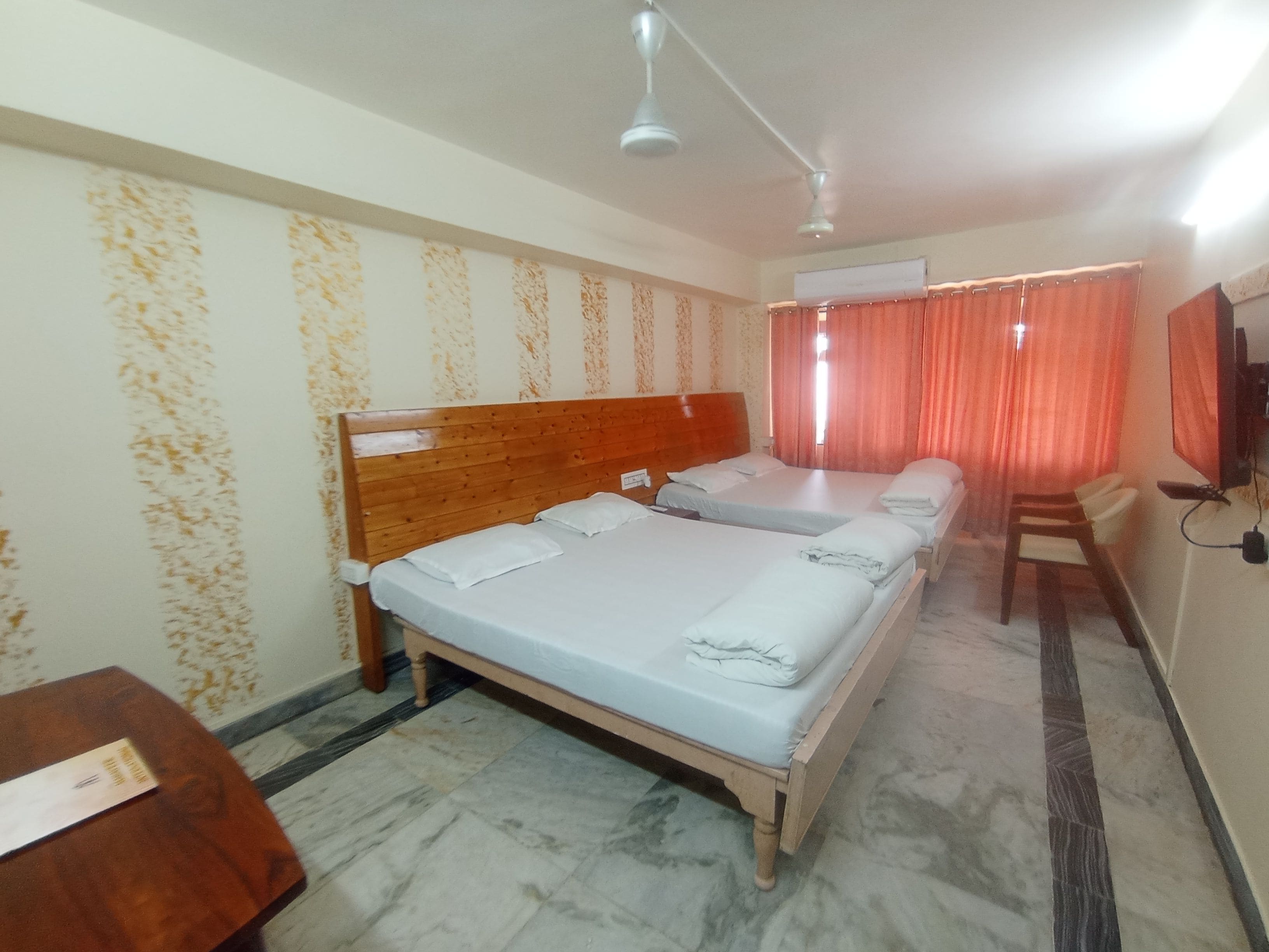 Habitación de hotel con dos camas, cabecero de madera, piso de mármol, escritorio, silla, televisor y ventana con cortinas.