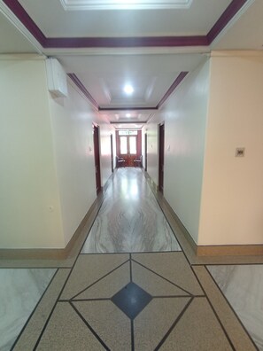 Een gang met een vloer met een geometrisch patroon, deuren aan beide kanten en een plafond met inbouwverlichting.