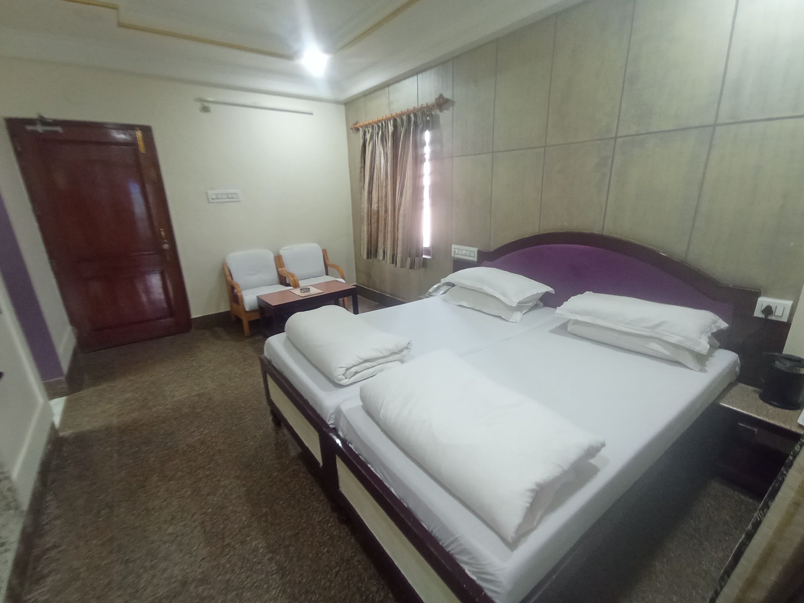 Una habitación de hotel con cama, sillón, mesita y puerta.