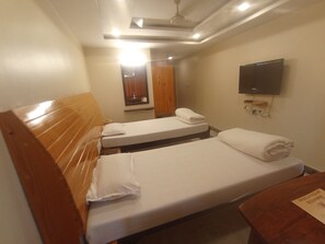 Habitación de hotel con dos camas individuales, cabecero de madera, televisor de pantalla plana montado en la pared y ventilador de techo.