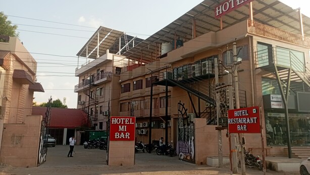 Um hotel com entrada coberta, vários andares e uma escadaria visível.