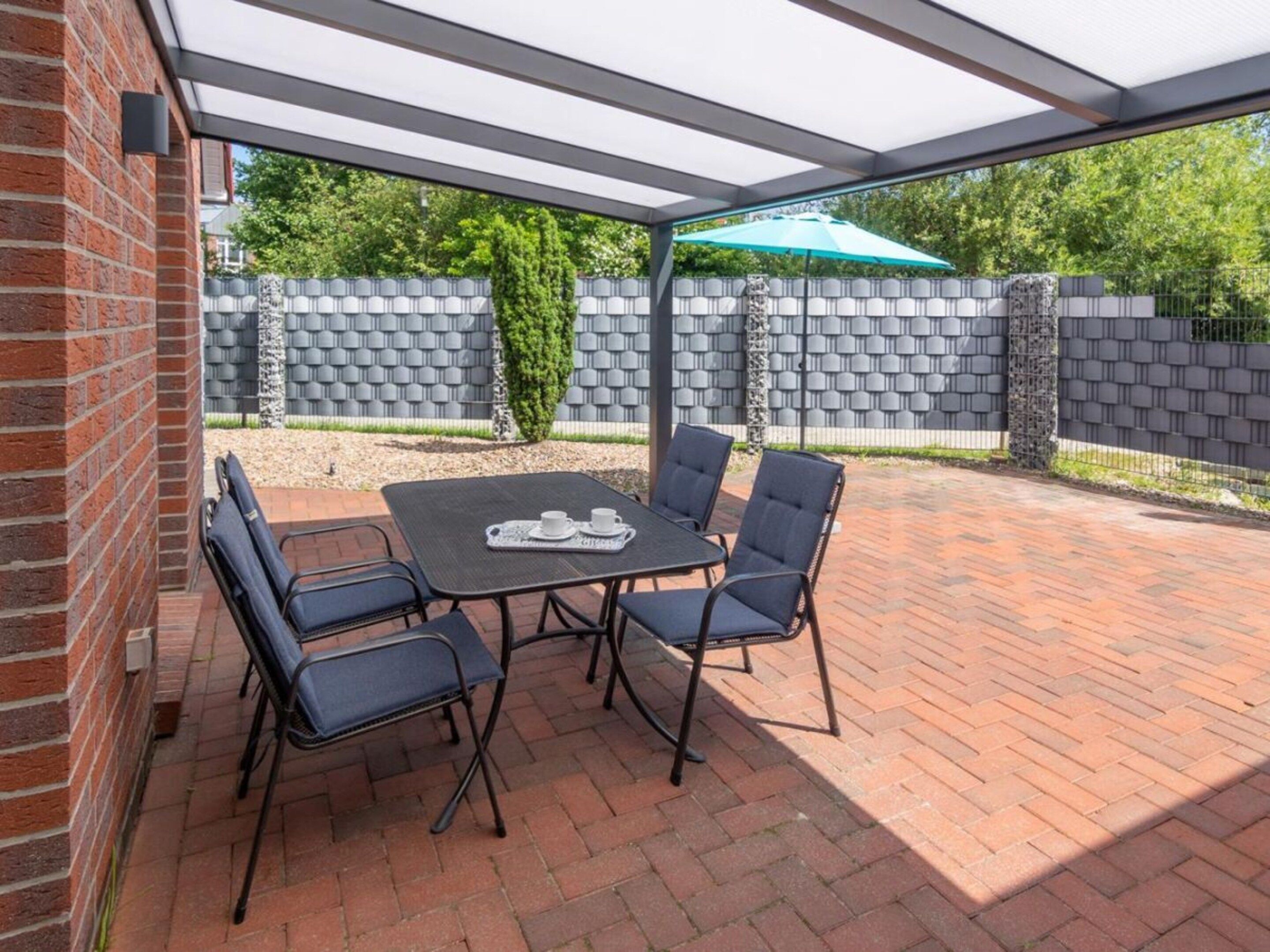 An outdoor patio with a table and chairs, a brick wall, and a green umbrella.