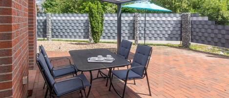 An outdoor patio with a table and chairs, a brick wall, and a green umbrella.