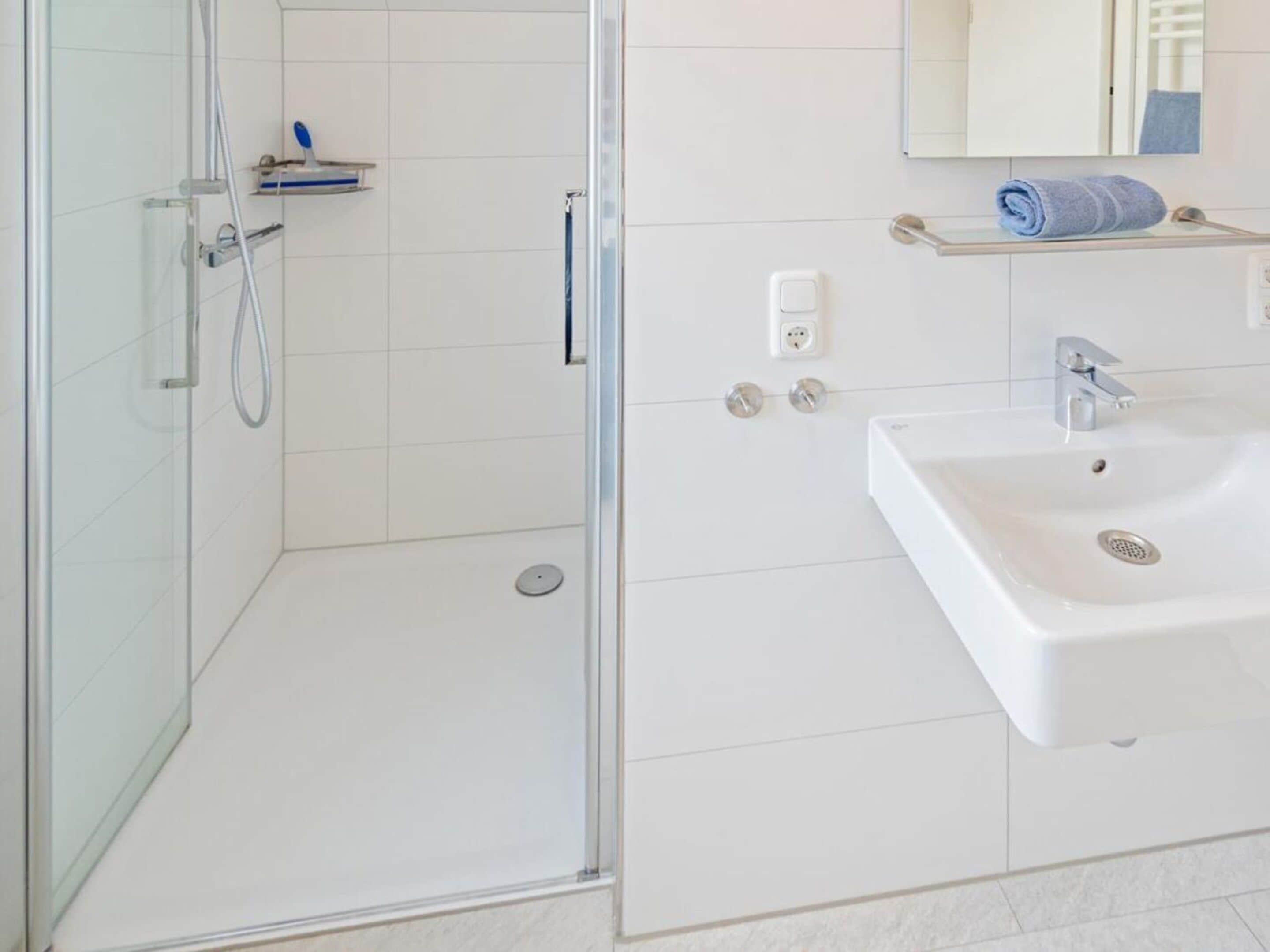 A modern bathroom with a glass-enclosed shower, a white sink, and a mirror above the sink.