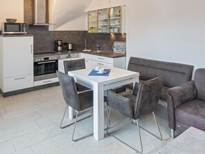 A modern kitchenette with a microwave, oven, and coffee maker. There is a dining area with a table and chairs. - Holiday Apartment With 1 Bedroom (Esens)