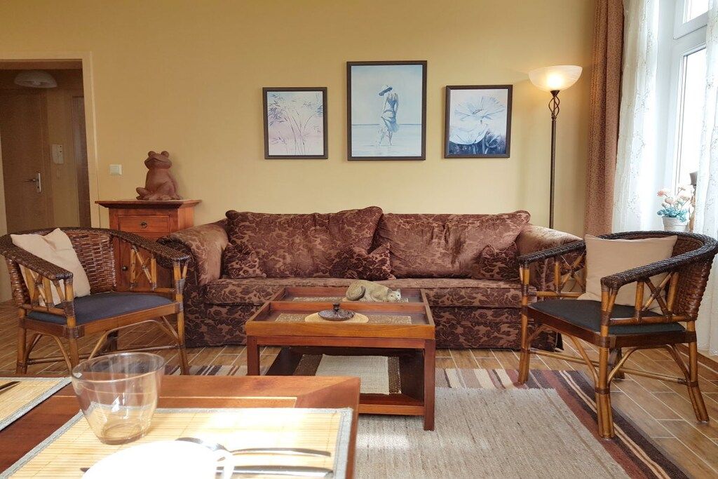 A living room with a sofa, two armchairs, a coffee table, and a lamp. There are three framed pictures on the wall.
