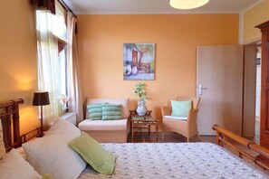 Un dormitorio con una cama, dos sillas, una mesa y un cuadro en la pared.