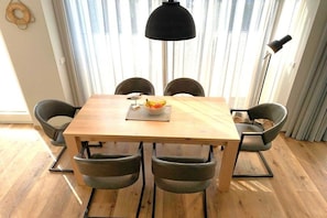 Ein Essbereich mit einem Holztisch, vier Stühlen, einer schwarzen Pendelleuchte und einer Obstschale.