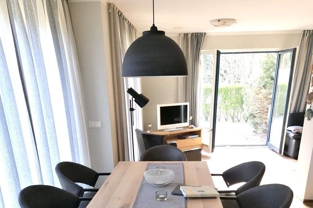Ein Essbereich mit Tisch, Stühlen, einer Pendelleuchte, einem Fernseher und Blick ins Freie.