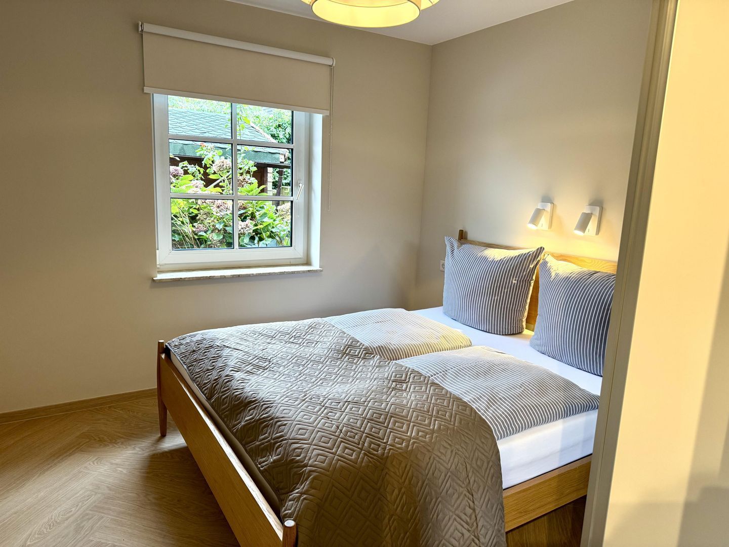 A bedroom with a bed, a window with blinds, and a view of greenery outside.