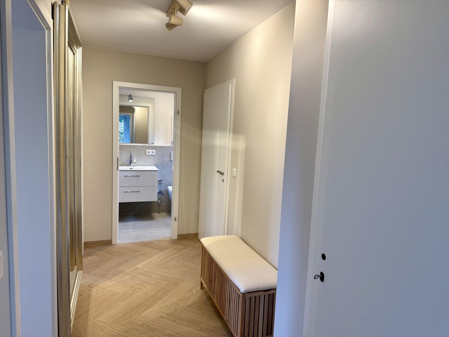 A hallway with a bench, a door, and a bathroom visible through an open door.