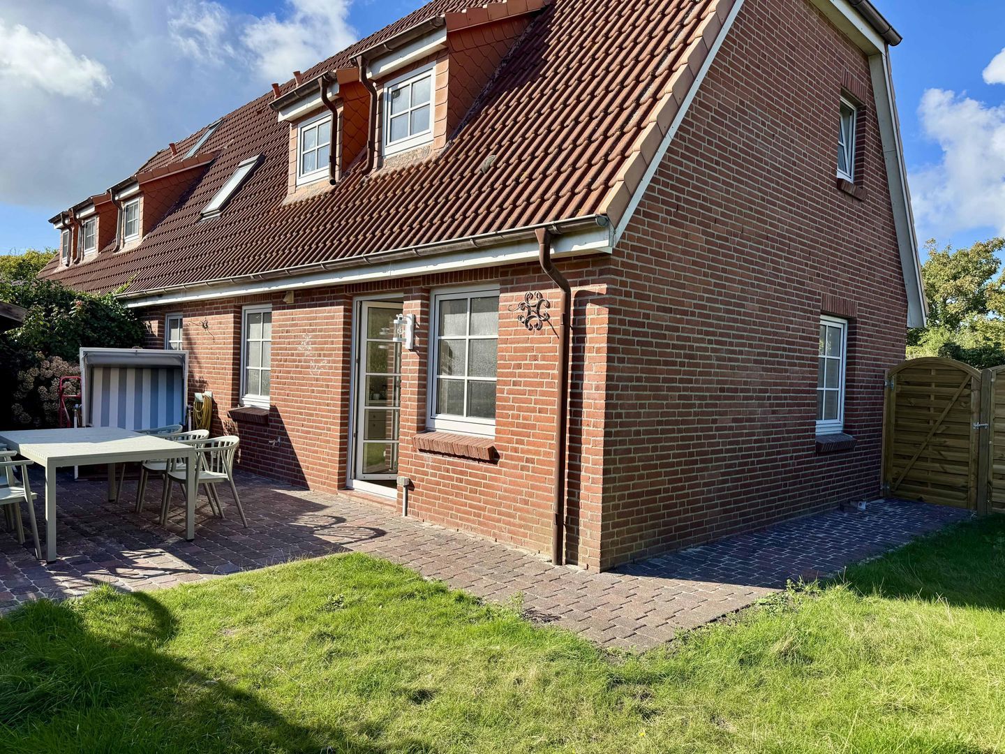 A two-story house with a brick exterior, a tiled roof, and a small front yard with a table and chairs.