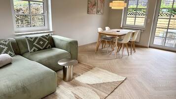 Ein modernes Wohnzimmer mit einer Eckcouch, einem Esstisch mit Stühlen und großen Fenstern.