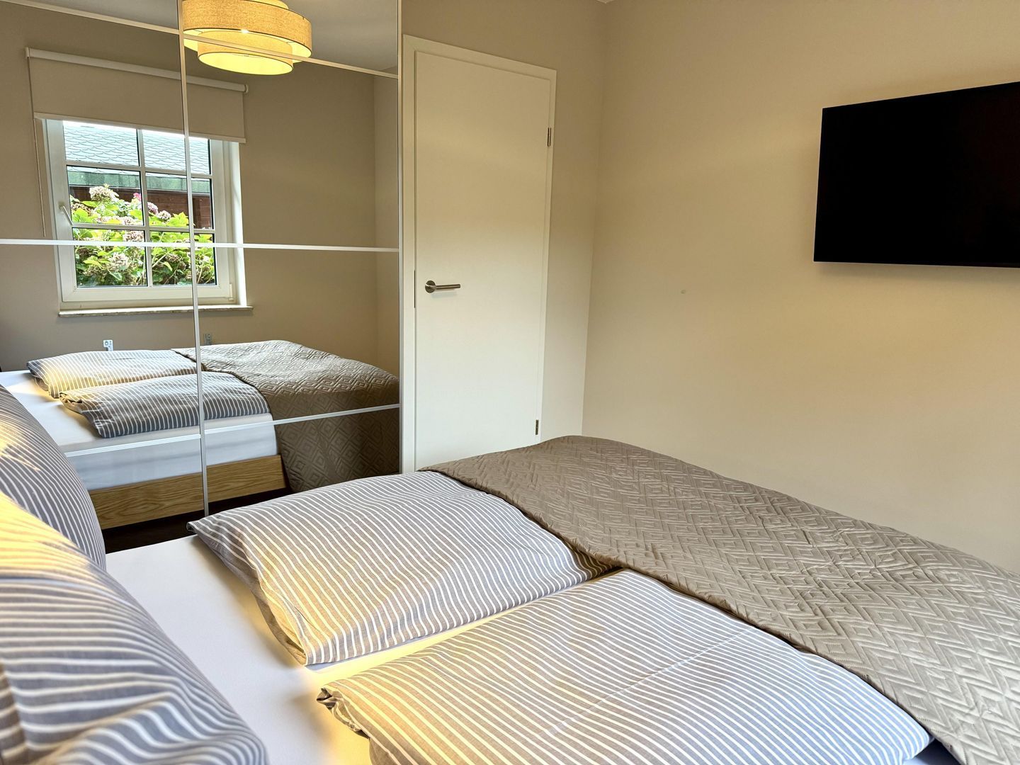 A bedroom with two beds, a window, a door, and a mounted TV.