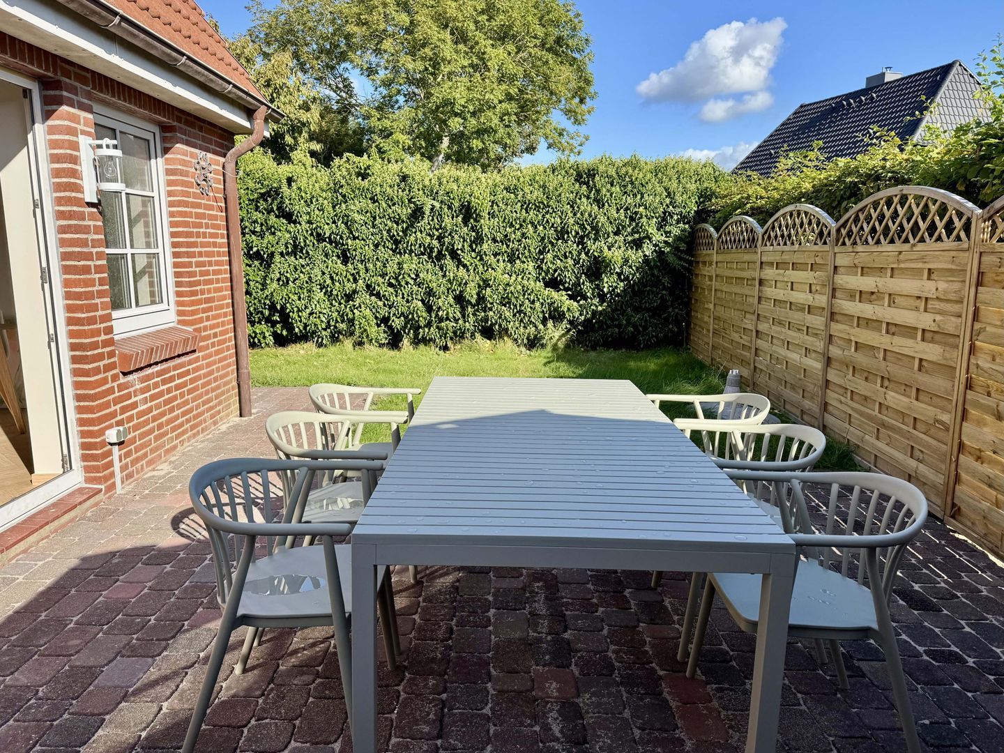 A patio with a table and chairs, a brick wall, a wooden fence, and a hedge.