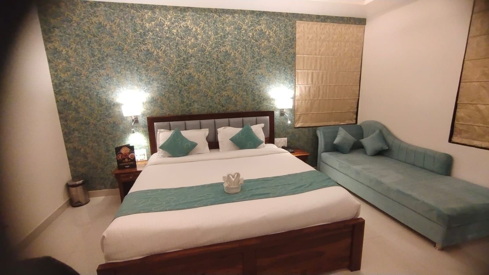 A bedroom with a bed, a nightstand, a lamp, a sofa, and a wall with a textured pattern.