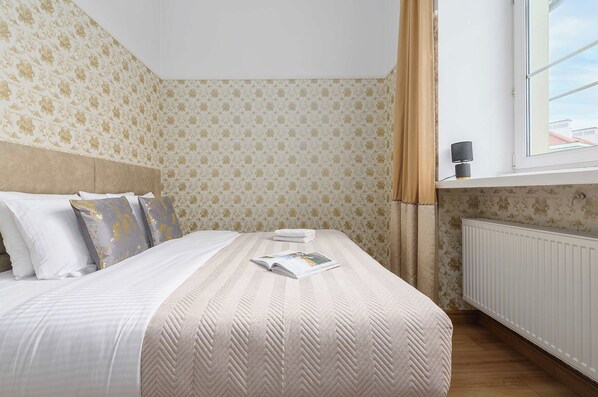 A neatly made bed with a patterned bedspread, a pillow with a floral design, and a magazine on the bed.