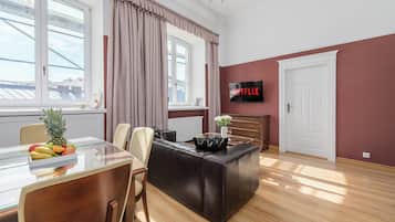 Un salon moderne avec une table à manger en verre, un canapé en cuir et un téléviseur à écran plat fixé au mur.