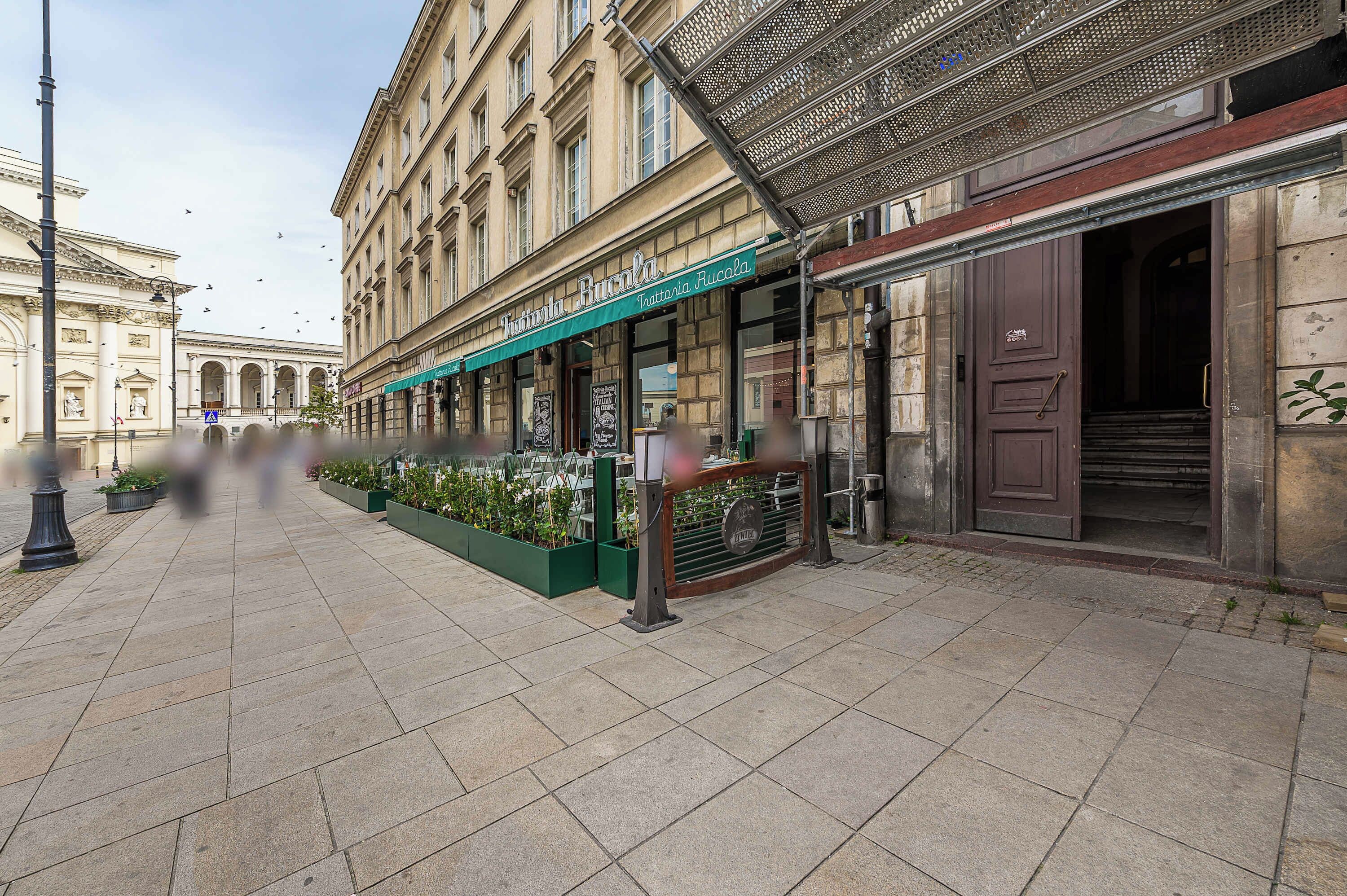 A street with a building featuring a restaurant named 'Tattoia Rucola' with outdoor seating and a green awning.