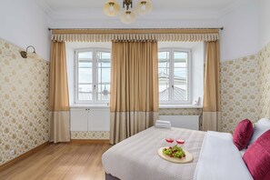 A hotel room with a large bed, a window with curtains, a radiator, and a wall with patterned wallpaper.
