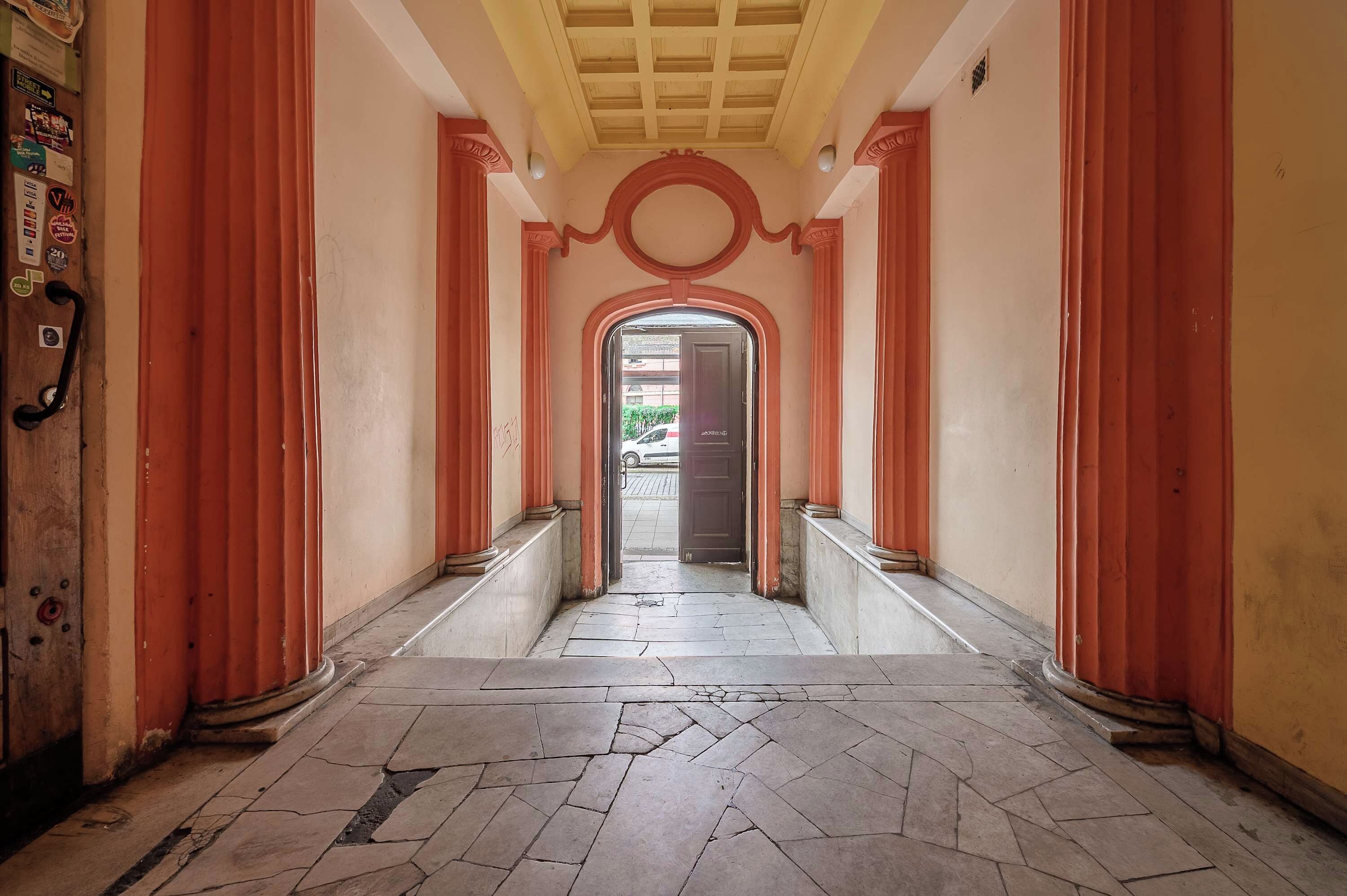 A corridor with a tiled floor, red columns, and a door at the end.