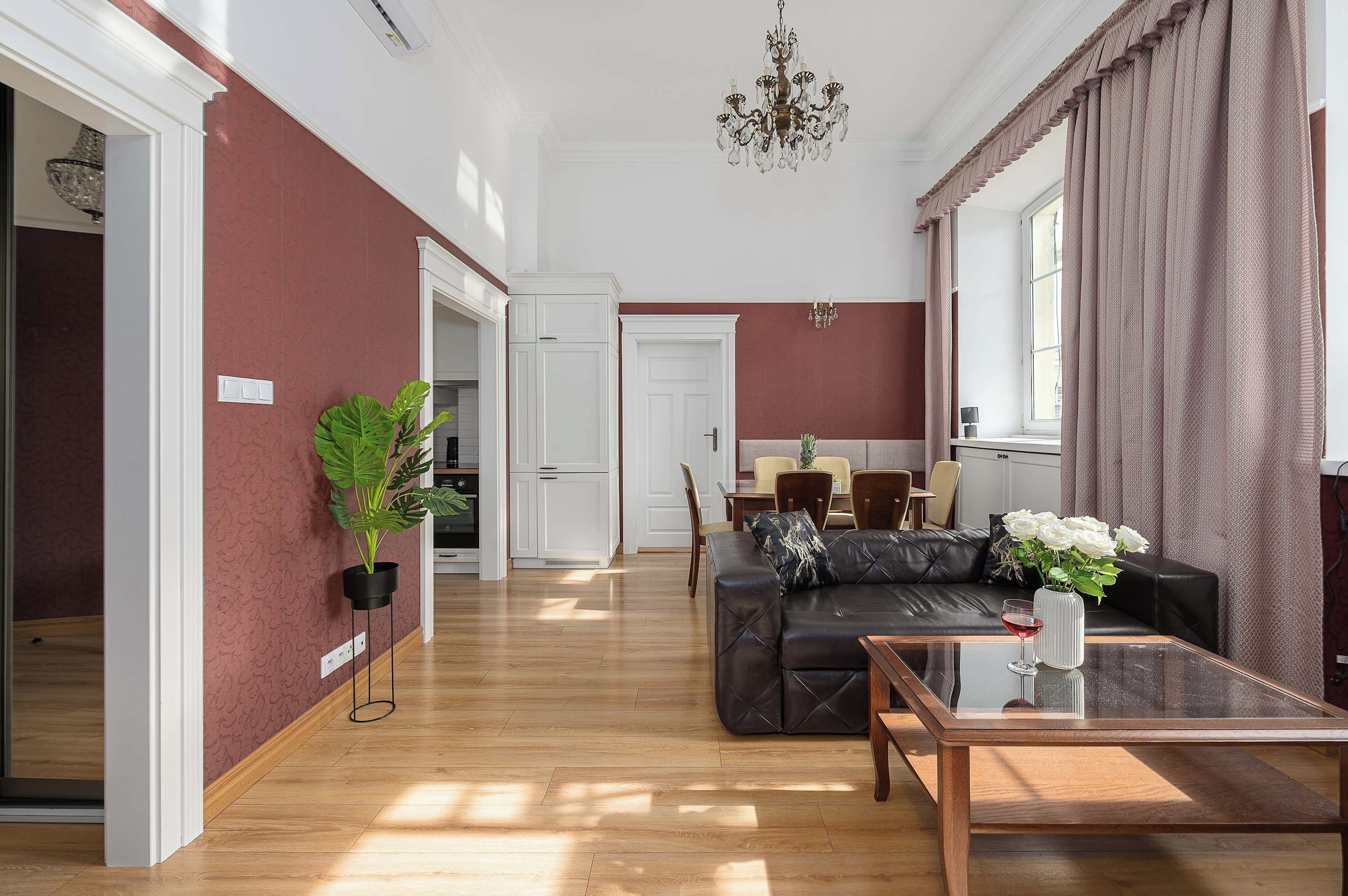Un salón amplio con un sofá de cuero negro, una zona de comedor con mesa y sillas, y un gran ventanal con cortinas.