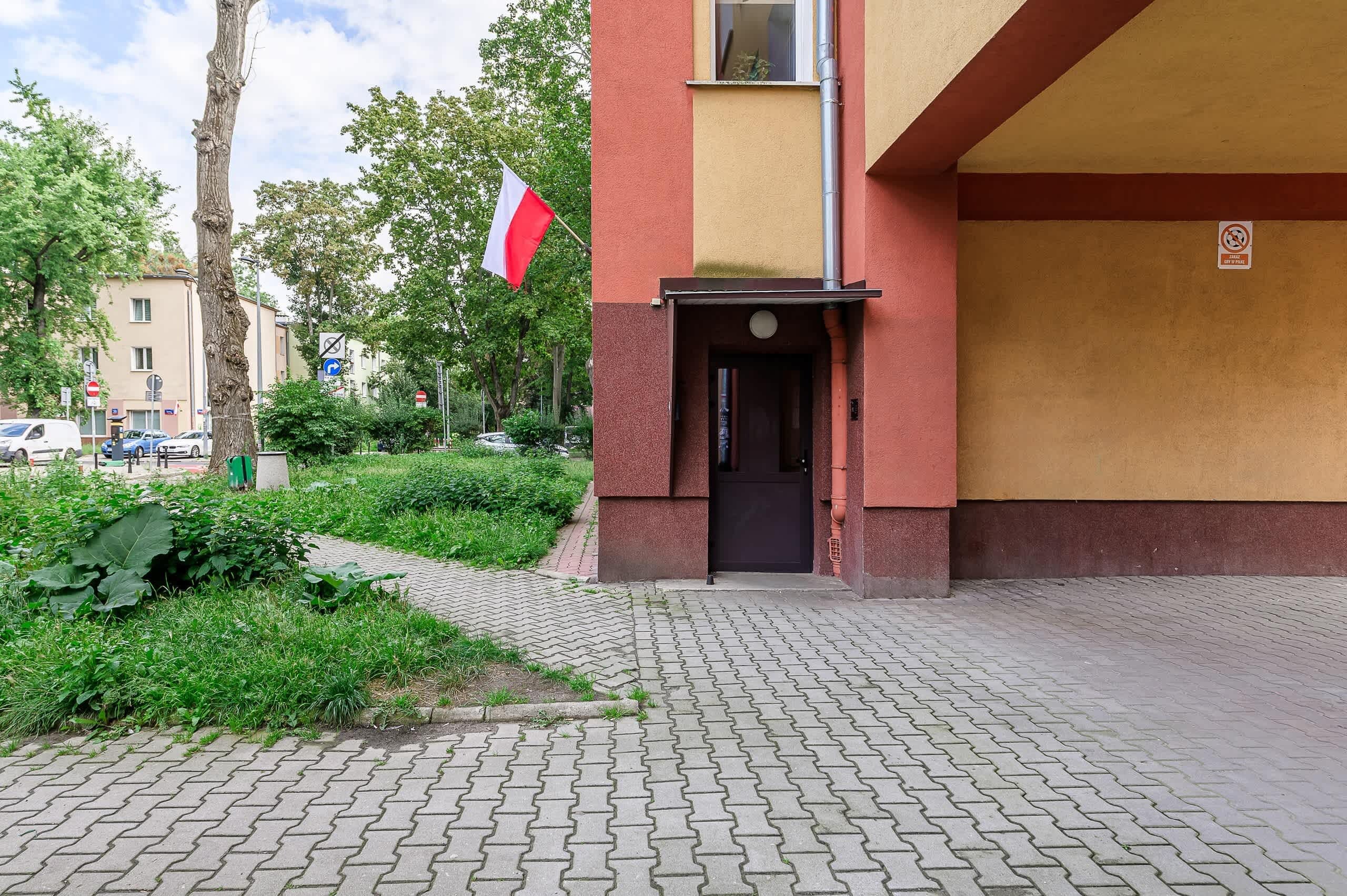 L'ingresso di un edificio con facciata rossa e gialla, una bandiera e il divieto di parcheggio.