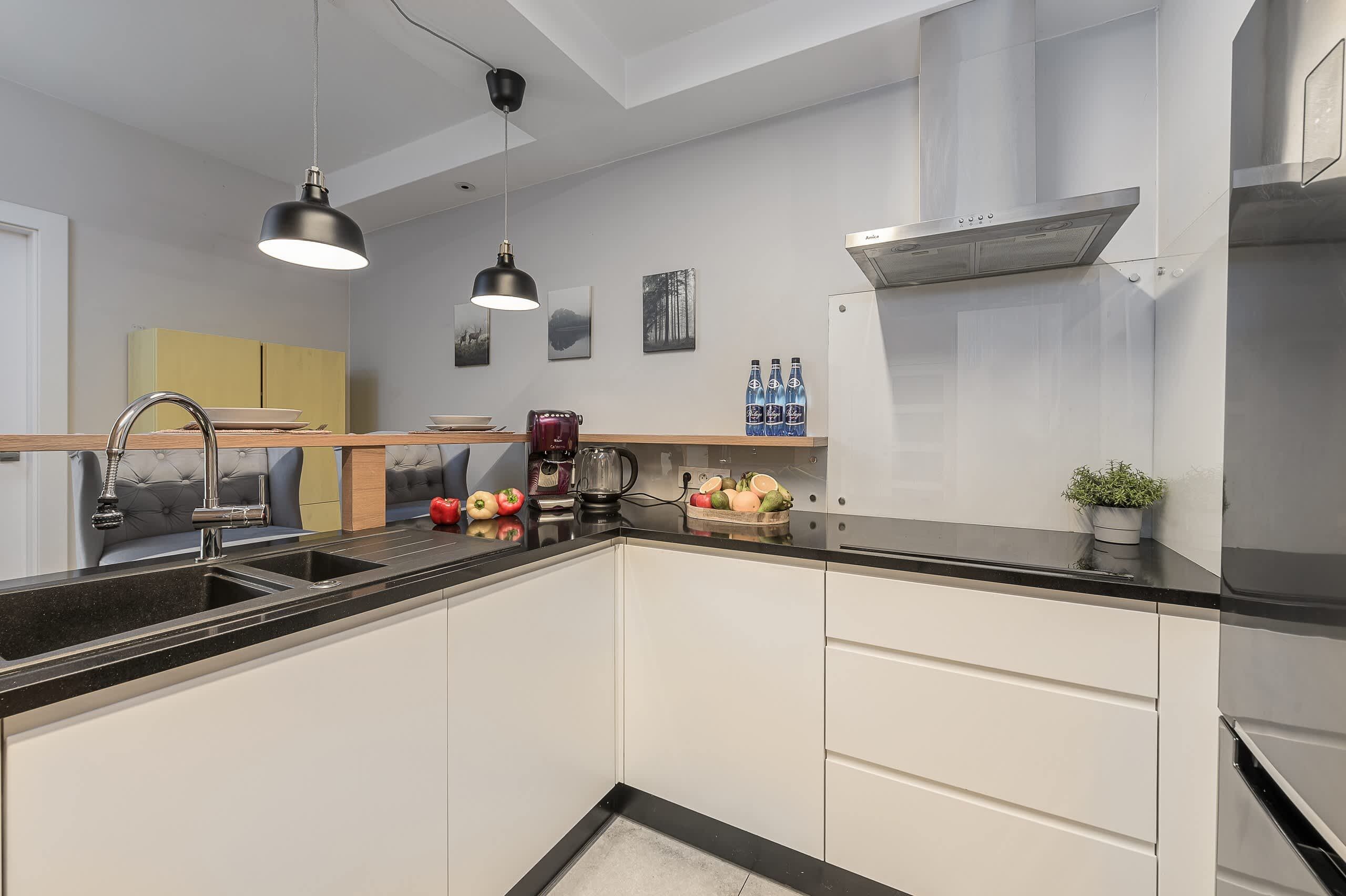 Une cuisine moderne dotée d’un plan de travail noir, d’appareils électroménagers en acier inoxydable et de luminaires suspendus.