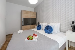 A modern hotel room with a large bed, a wooden wardrobe, a white bedside table, and a geometric patterned wall.