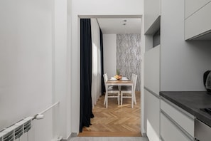 A narrow hallway leading to a dining area with a table set for two, a patterned wall, and a kitchen area with cabinets.