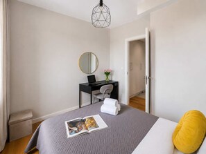 A bedroom with a bed, a desk, a chair, a round mirror, and a door leading to another room. - Lumina 3-room Apart w/ Parking & AC & Balcony (Warszawa)