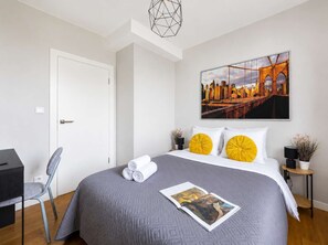 Ein Hotelzimmer mit einem Bett, einem Schreibtisch, einem Stuhl, einer Tür und einem an der Wand hängenden Kunstwerk.
