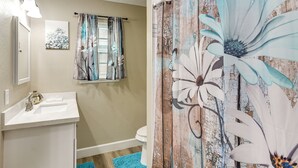 Un baño con lavamanos blanco, inodoro y cortina de ducha con diseño floral.