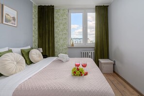 A hotel room with a bed, a window with a view, and a small table with a fruit arrangement. - Lumina 4-room Apart with Balcony near Metro (Warszawa)