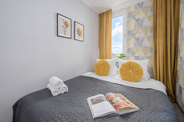 Ein Hotelzimmer mit Bett, einem Vorhangschieberfenster, einer Wand mit Kunstwerk und einer Zeitschrift auf dem Bett.