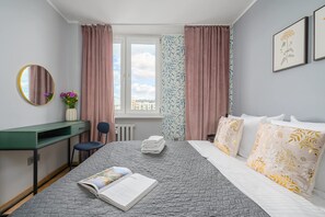 A hotel room with a bed, a desk, a chair, a window with curtains, and a framed picture on the wall. - Lumina 4-room Apart with Balcony near Metro (Warszawa)