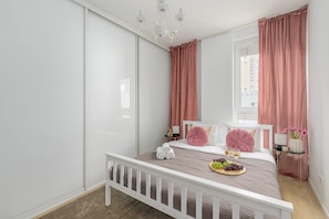 Un dormitorio con una cama, una mesita de noche, un candelabro y una ventana con cortinas.