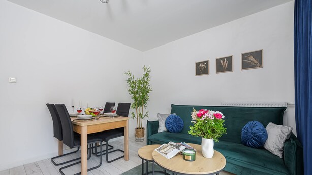 A modern living room with a dining area, a green sofa with decorative pillows, a small round table, and a potted plant. - Lumina 2BR Apart w/ Parking I Center I Balcony (Łódź)