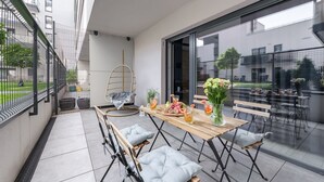 A modern outdoor dining area with a wooden table, cushioned chairs, and a glass partition. - Lumina 2BR Apart w/ Parking I Center I Balcony (Łódź)