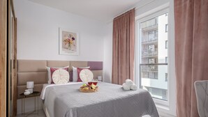 A hotel room with a bed, a nightstand, a lamp, a framed picture on the wall, and a window with curtains. - Lumina 2BR Apart w/ Parking I Center I Balcony (Łódź)