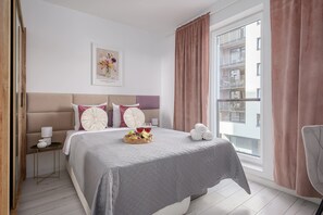 Ein Hotelzimmer mit einem Bett, einem Nachttisch, einer Lampe, einem gerahmten Bild an der Wand und einem Fenster mit Vorhängen.