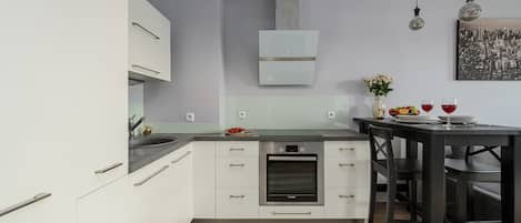 Una cocina moderna con armarios blancos, un horno Bosch, un comedor con mesa y sillas negras, y una obra de arte con motivos urbanos en la pared.