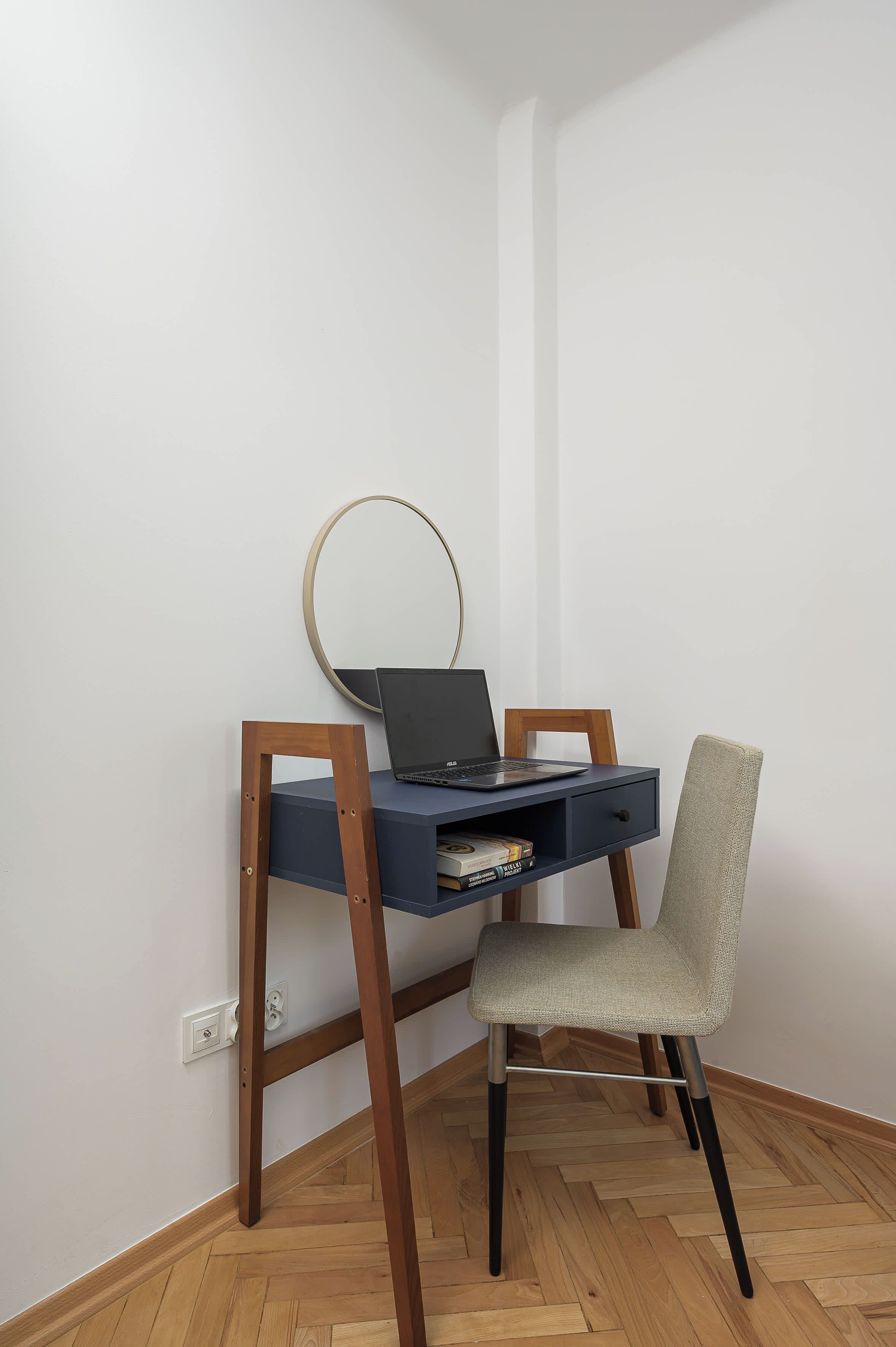 Een hoekbureau met een laptop, een stoel en een spiegel aan de muur.