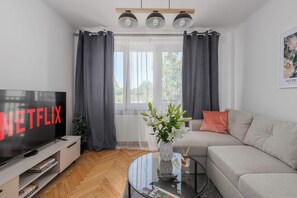 A living room with a flat-screen TV, a sofa, a glass coffee table, and a window with curtains. - Lumina 3-room Apart w/ Balcony near Park & Metro (Warszawa)